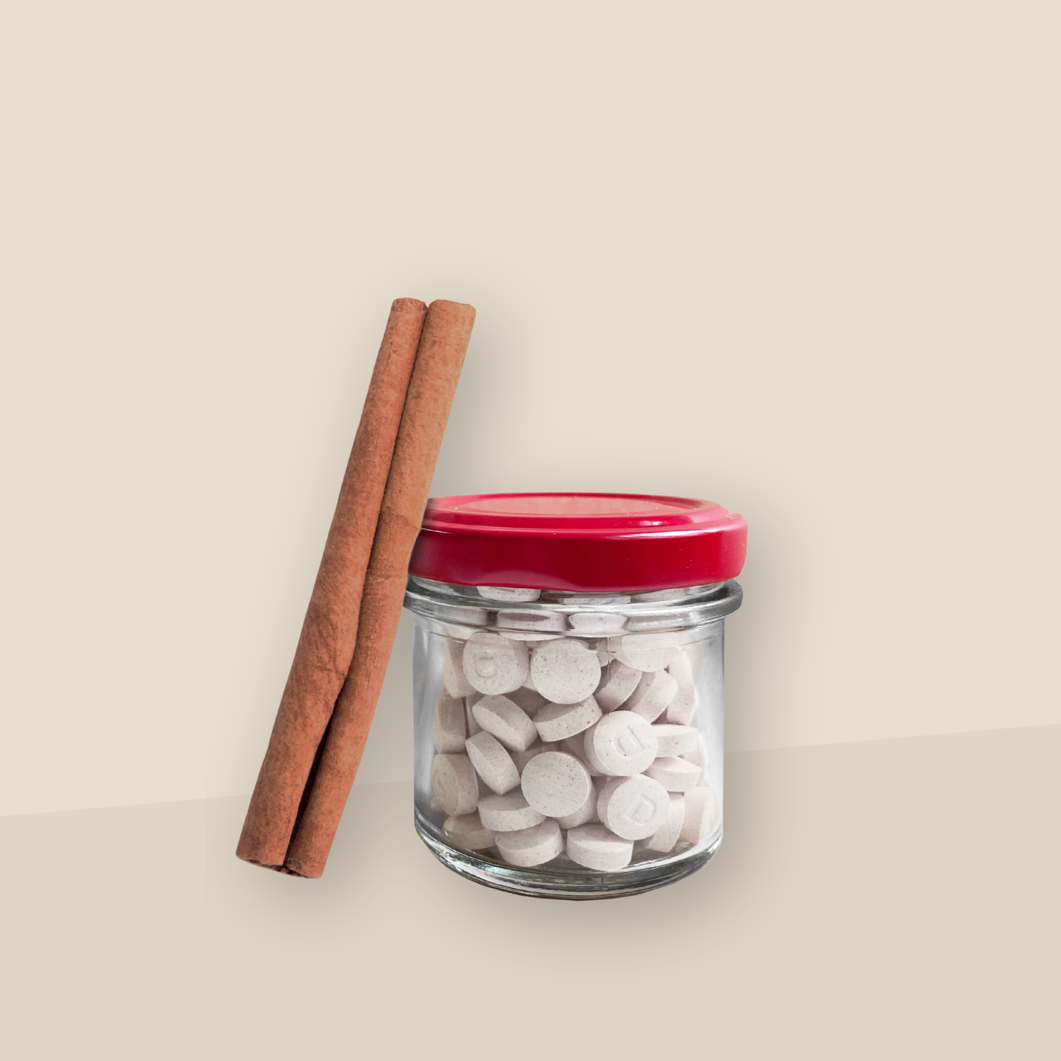Ein Aufbewahrungsglas mit rotem Deckel gefüllt mit Denttabs in Zimtgeschmack. Eine Zimtstange lehnt an dem Glas. Der Hintergrund ist beige.